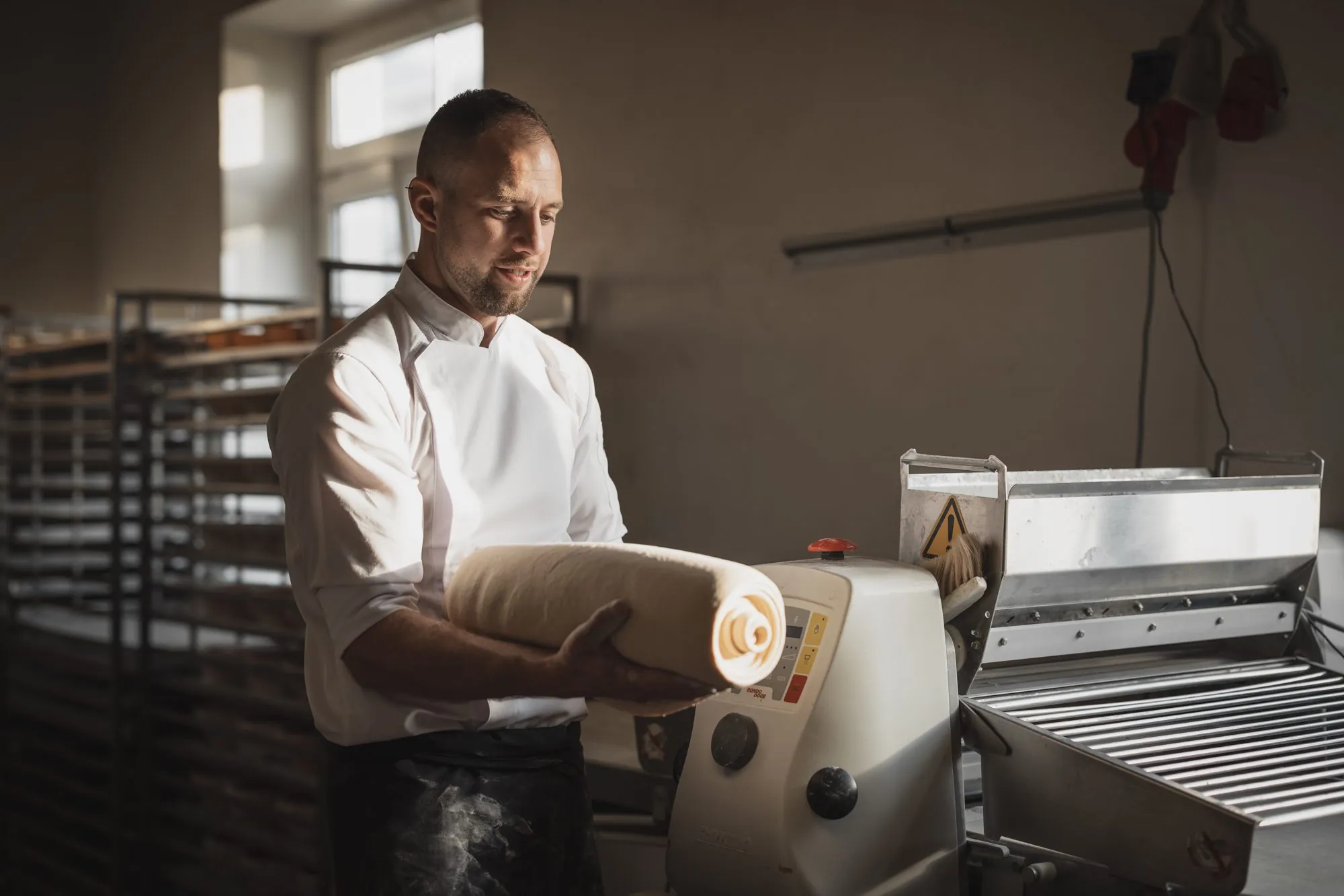 Bäcker an der Teigmaschine in der Backstube der Brotschmiede