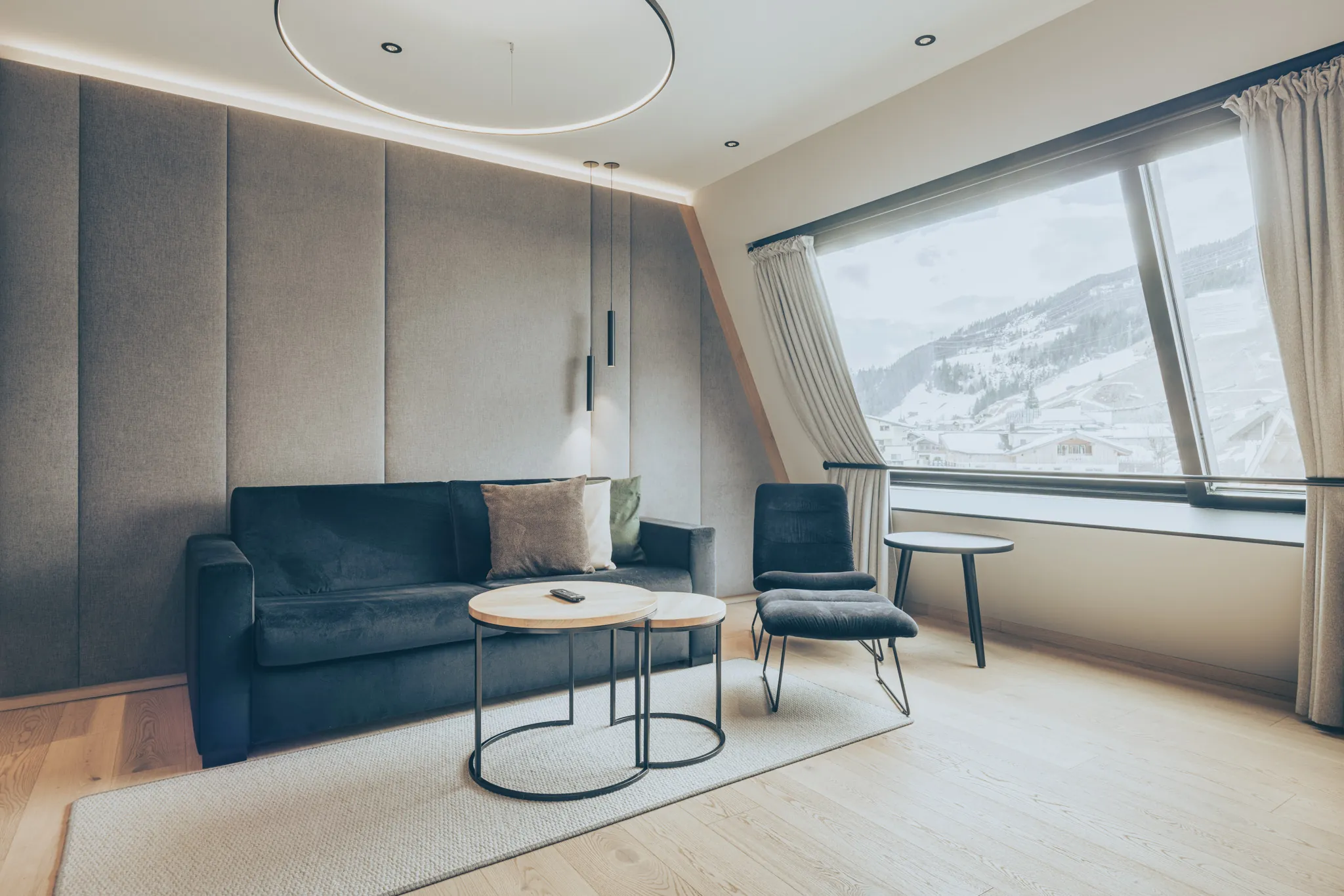 Zimmer im DAS GERLOS mit Sofa, Sessel und großem Fenster auf die verschneiten Hänge