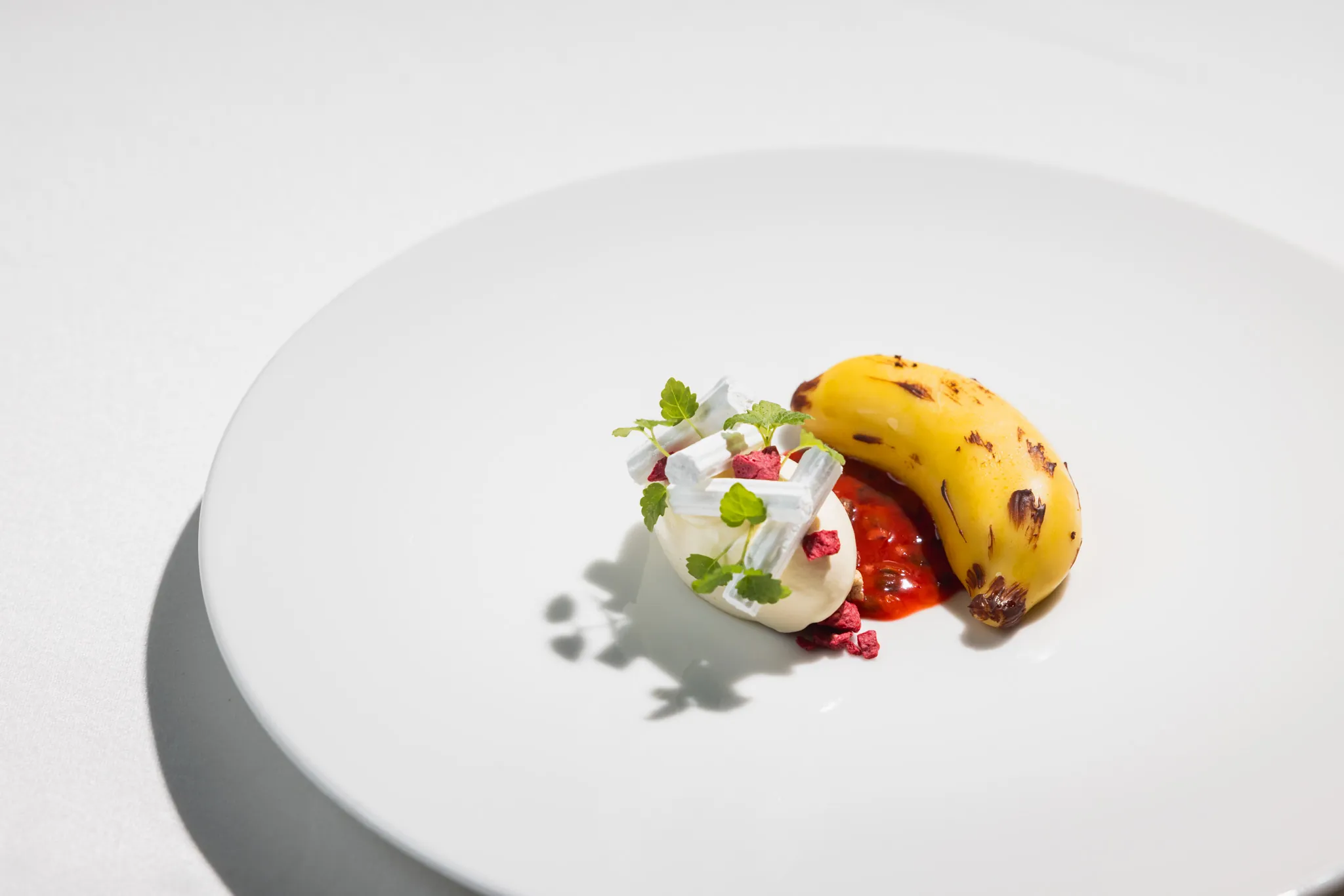 Dessert mit gebrannter Banane, roten Beeren und Creme im Tageslicht
