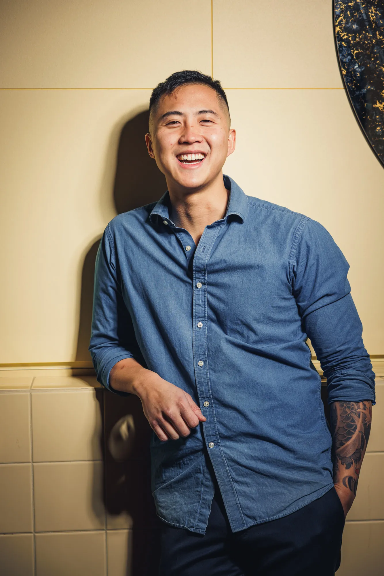 Lachender Mitarbeiter im Jeanshemd lehnt an der Wand, Teamportrait für das Restaurant CONG in Stockholm