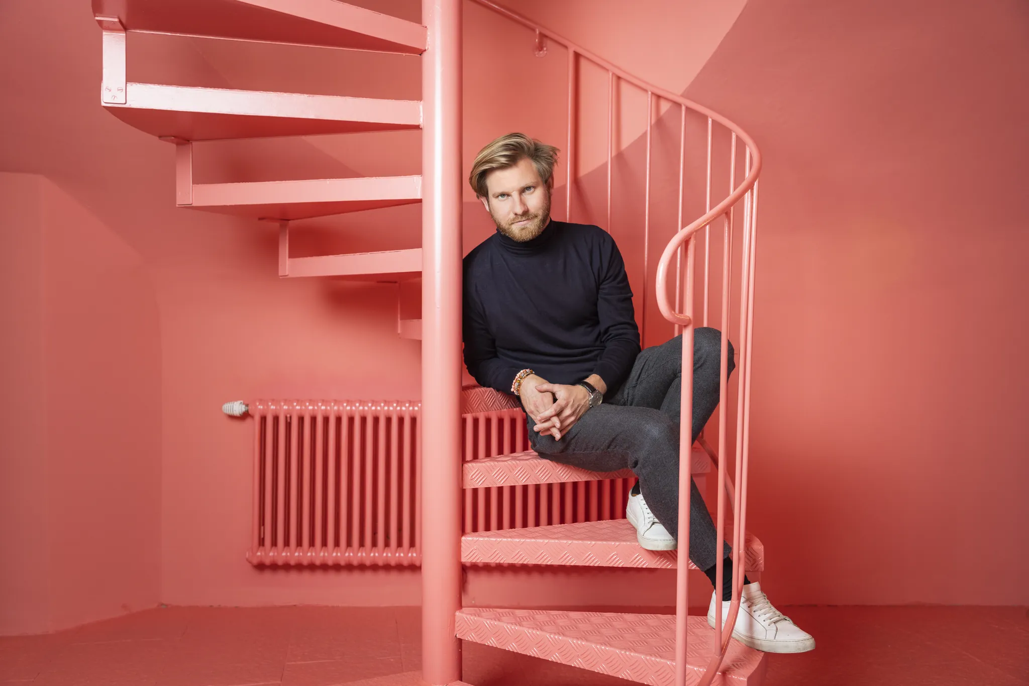 Mann auf einer rot gestrichenen Wendeltreppe in komplett rotem Raum, Business Portrait on Location
